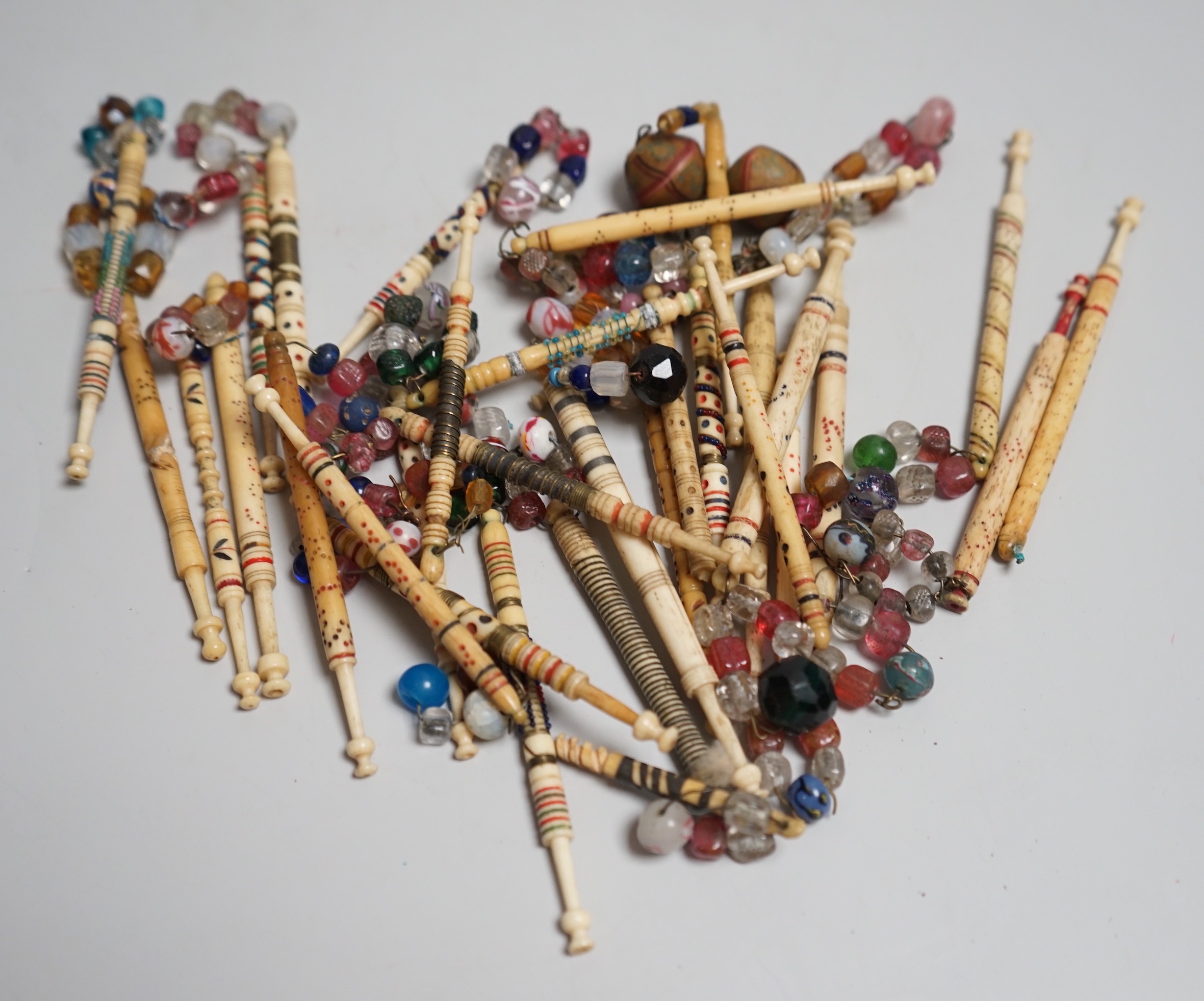 Twenty 19th century ornately decorated lace bobbins with glass bead tops and eleven carved bobbins with indistinctly carved surnames and names